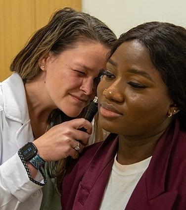 Nursing student looks in the ear of a patient